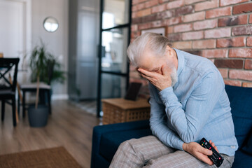 Side view of excited disappointed gray-haired senior man fan sitting at TV screen on sofa at home and watching online football supporter soccer, worry about losing match sport game.