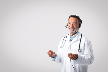 Smiling european senior doctor in white coat with stethoscope and headphones on gray background