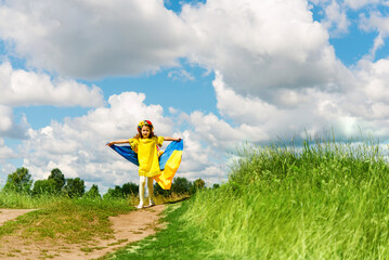 Ukrainian child girl wearing national clothes with embroidery and wreath of flowers holding flag of Ukraine outdoor. Ukraines Independence, Flag Day, Constitution day.