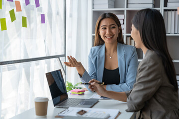 Two Asian businesswoman discussing startup projects, concepts, analyzing planning, financial statistics and investment markets from chart documents. Data notebook and laptop happily in the office.