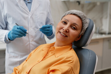 Portrait of smiling senior woman in dental clinic sitting in chair and looking at camera