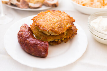 Fried grated potato pancakes with fried sausage on white plate