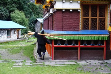 A devoted pilgrim performs Tibetan circumambulation at Hinang monastery, carrying two long logs...