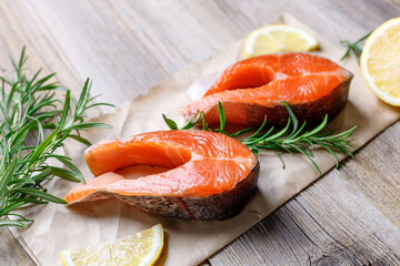 Steak of fresh raw red fish salmon with lemon, rosemary and pepper on wooden background