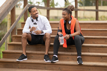 Tired positive young black family in sportswear sit with bottles of water rest after jogging in...
