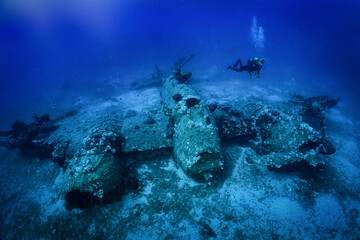 A scuba diver explores a sunken world war two fighter propeller airplane at the seabed of the...
