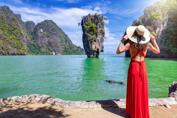 Fototapeta na wymiar A tourist woman in a red dress looks at the famous sightseeing spot James Bond island at Phang Nga Bay, Phuket, Thailand