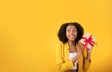 Ideas for gift. Excited glad black woman holding gift box and looking at blank space isolated on...