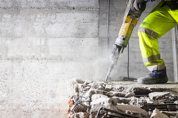 Construction worker using heavy-duty jackhammer tool and breaking reinforced concrete. Demolishing...