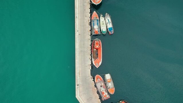 A drone flies over a fishing village, giving a top down view of the dock and boats. The boats are moored in a row.