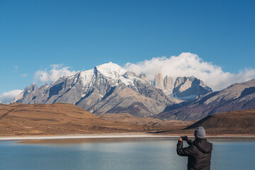 A man tourist in black jacket and a hat taking a picture of the view of Laguna Amarga, mountains in...
