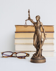 Themis goddess of justice statuette on light background on table with books and glasses. legal company, university judicial structure. bar association and human rights defenders, court acquittal
