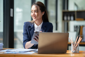 Asian businesswoman in a suit sitting holding iPad or tablet in contact See details and discuss business information happily in the office.