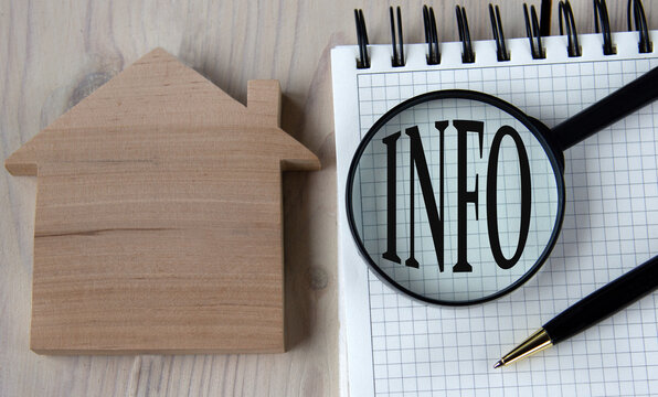 The word INFO under a magnifying glass on a white notebook against the background of a wooden house and banknotes - Powered by Adobe