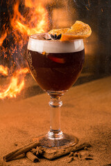 Alcoholic cocktail of beer, champagne and liqueur with orange and anise in a glass on a table sprinkled with powdered cinnamon with fire and sparks.