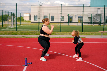 Obraz premium Mother and daughter play sports together in the open area of the stadium. The girl supports her mom by keeping her company in fitness classes