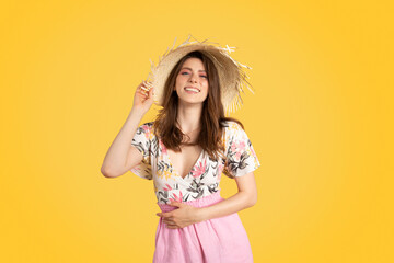 Pretty european lady in colorful summer outfit and straw hat, posing on yellow background and...