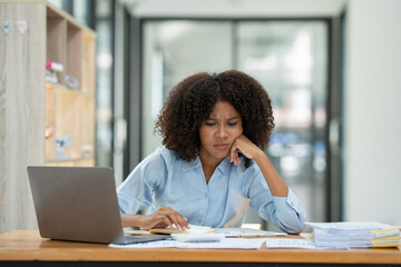 Young American businesswoman working on the laptop with documents and stressing at work from working on financial documents in office Overworked woman concept.