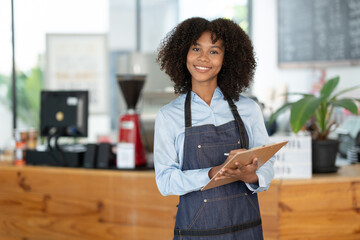 Beautiful african american female cashier or barista writing purchase details and checking...