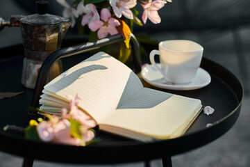 Cup of coffee flowers and notebook on the small black table