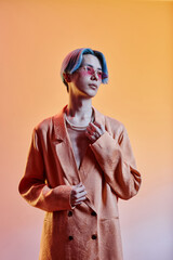 Vertical image of stylish guy with blue hairstyle and trendy jacket standing against colored...