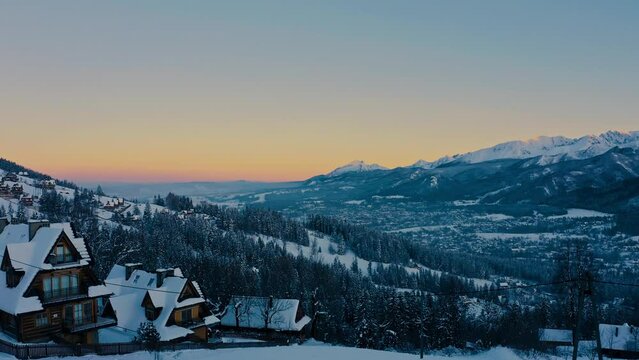 Stunning Drone Aerial Shot during sunset above winter trees and houses covered in snow