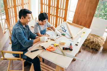 Happy Asian father and son work as a woodworker and carpenter. Father teaching his son to hammer...