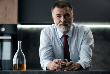 Confident rich mature wealthy businessman chilling relaxing drinking enjoying whiskey in the kitchen after work.