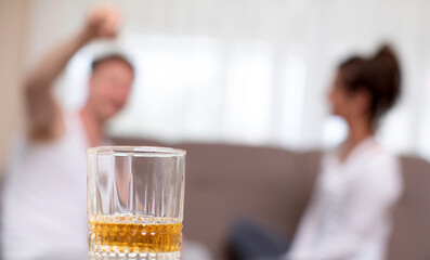 Alcoholism and relationship problems concept. Depressed mature woman grabbing her head, being afraid of domestic violence, husband drinking alcohol 
