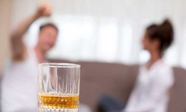 Alcoholism and relationship problems concept. Depressed mature woman grabbing her head, being afraid of domestic violence, husband drinking alcohol 
