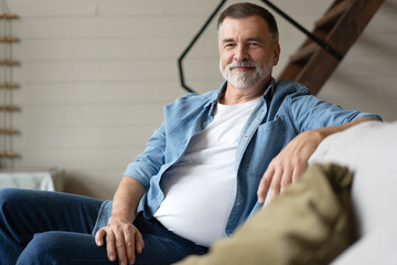 Happy mature man sitting on couch. Portrait of man relaxing at home with big smile.