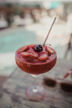 Red cocktail garnished with strawberries on a poolside