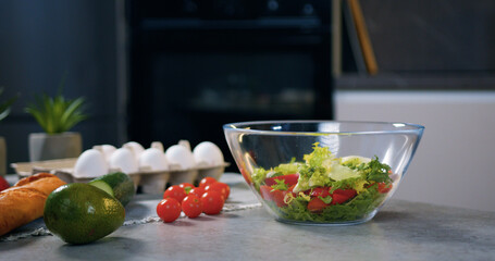 Fresh nutritious small pieces of lettuce falling into transparent bowl where are cherry tomatoes that prepared for vitamin nutritious salad
