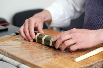 Hands of a chef rolling white asparagus in nori seaweed leaves on a kitchen board, cooking preparation for a vegetarian gourmet dinner, selected focus