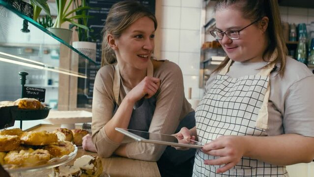 Down syndrome girl and her female workmate using digital tablet to check the commodity of the bakery. Shot with RED helium camera in 8K. 