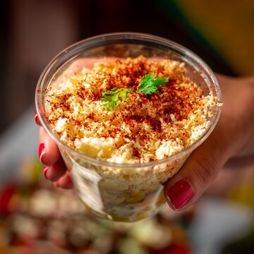 Hand holding a fresh mexican esquite filled with cheese, pepper, and fresh vegetables on the go