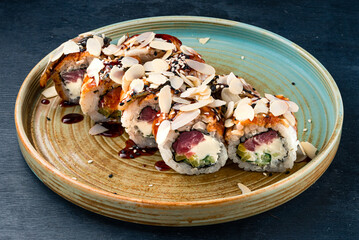 Sushi rolls with tuna, cream cheese, cucumber, almonds, sesame seeds and barbecue sauce in a plate.