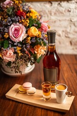 Pile of tasty macarons and brandy bottle with espresso shots ready for tasting in a fancy table decorated with flowers 