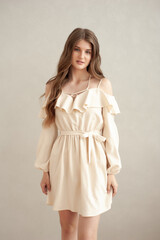 Beautiful young smiling woman portrait with wavy hair, dressed in a beige dress posing in the interior 