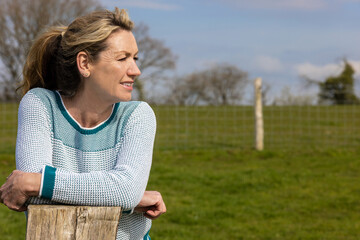 Attractive Thoughtful Middle Aged Woman Resting on Wooden Fence Post