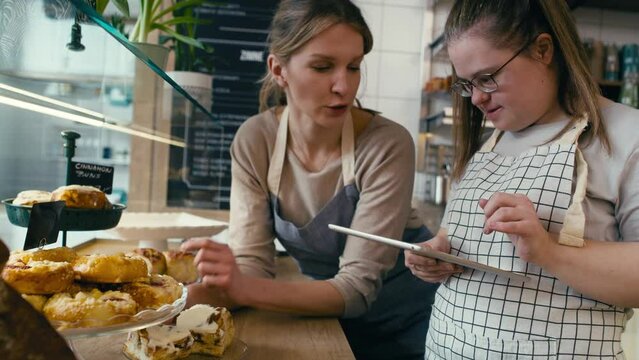 Down syndrome girl and her female workmate using digital tablet to check the commodity of the bakery. Shot with RED helium camera in 8K. 