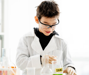 School boy wearing protection glasses with dirty face doing chemistry experiment with chemical liquids in elementary science class. Clever pupil analyzing results of test in lab