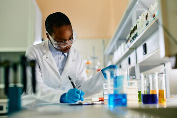 Black female biotechnologist taking notes during scientific experiment in laboratory.