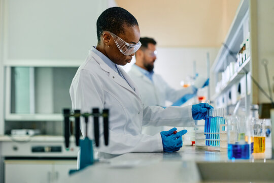 Black female lab technician analyzing liquid in test tubes during scientific experiment.