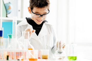 School boy wearing protection glasses with dirty face doing chemistry experiment in elementary science class. and measuring colorful liquids Clever pupil in lab