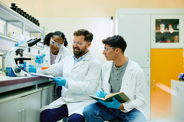 Obraz premium Happy chemist and his younger colleagues analyzing liquid in beaker in laboratory.