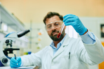 Close up of biochemist working with red liquid sample in laboratory.