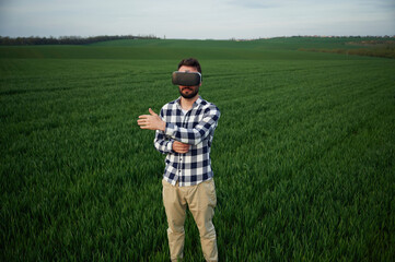Naklejka na ściany i meble Playing game in VR glasses. Handsome young man is on agricultural field
