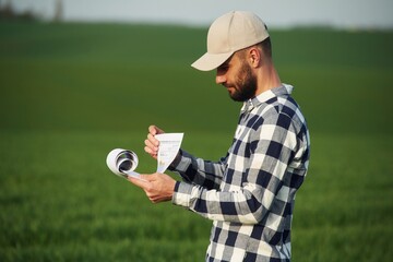 Worker is reading the document. Handsome young man is on agricultural field