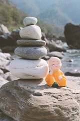 A small buddha or monk meditates near a cairn.